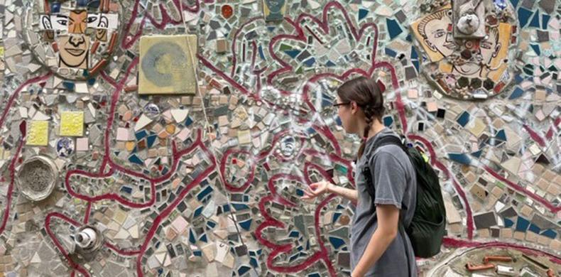 A students stands in front of a mosaic in Philadelphia.